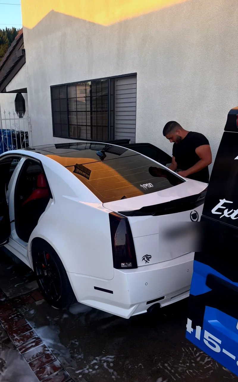 A Shine Bros detailer finishing a white Cadillac CTS-V on a driveway at sunset.