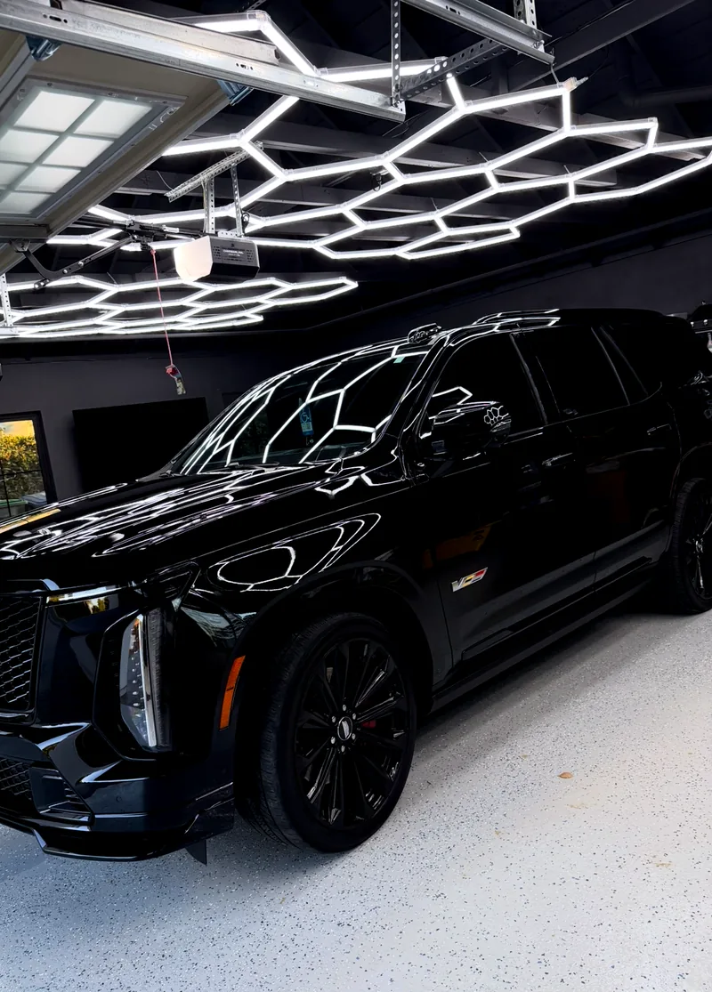 A black Escalade under workshop hex lighting, the lights reflected in unbroken lines across the paint.